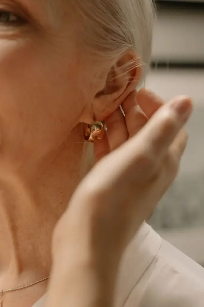 Woman adjusting a gold earring on her earlobe